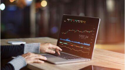 Persona analizando datos del mercado de valores en una computadora portátil. Se muestra 1052.34.