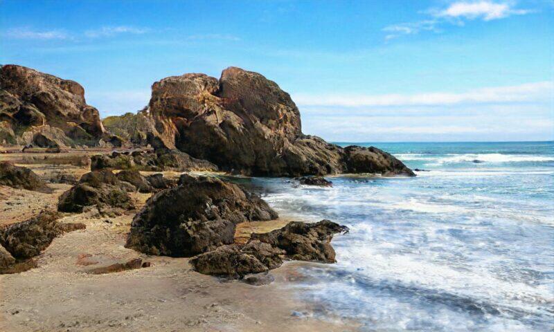 Las escarpadas rocas costeras se encuentran con las olas turquesas del océano en un día soleado.