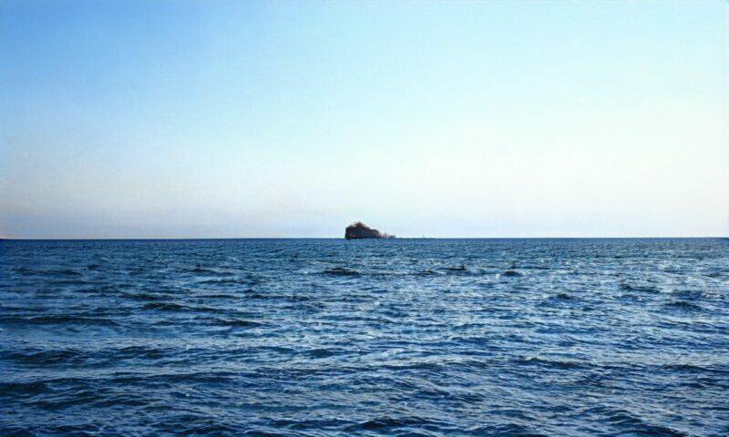 Isla solitaria en un océano en calma bajo un cielo azul claro.