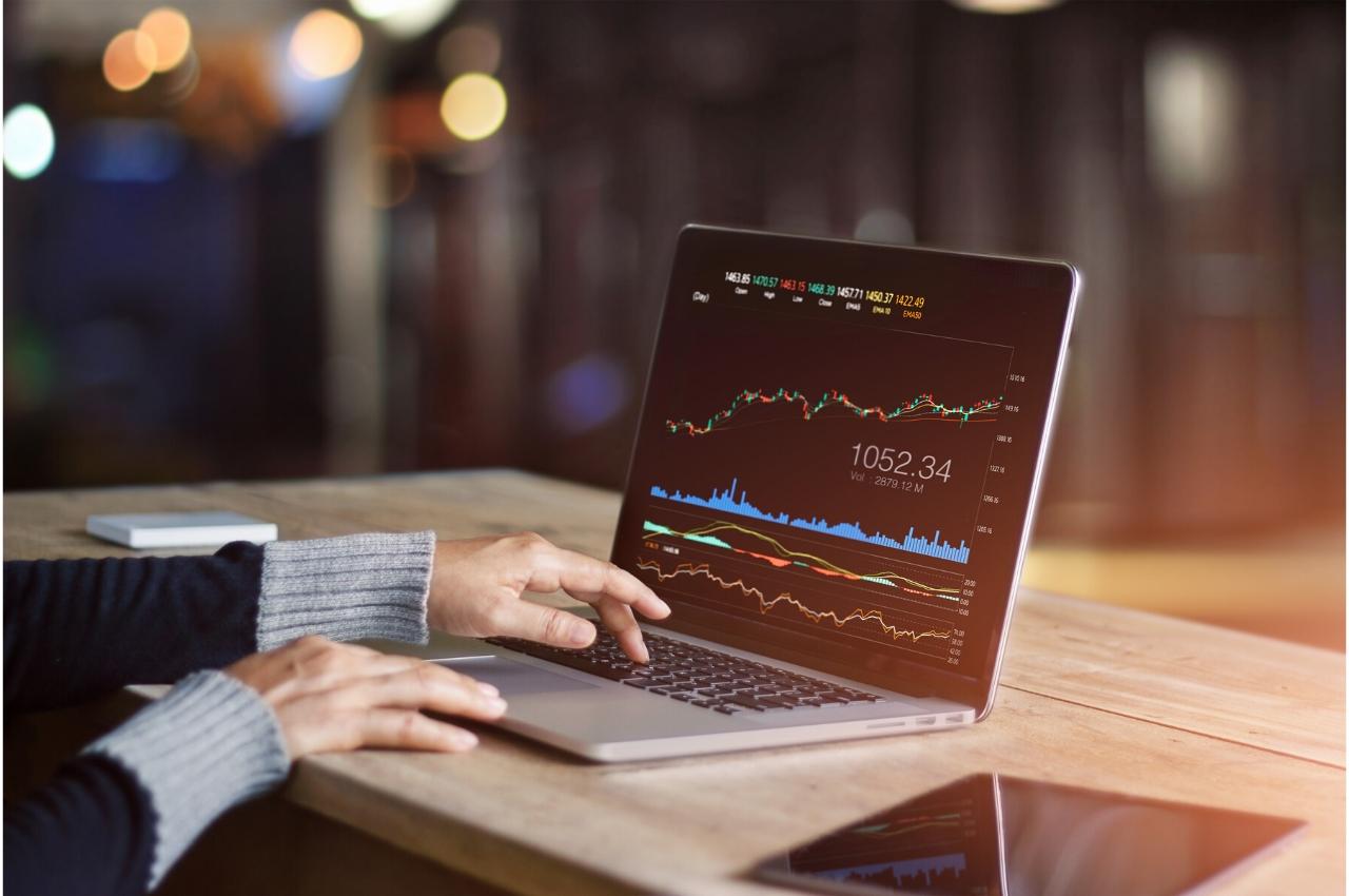Persona analizando datos del mercado de valores en una computadora portátil. Se muestra 1052.34.