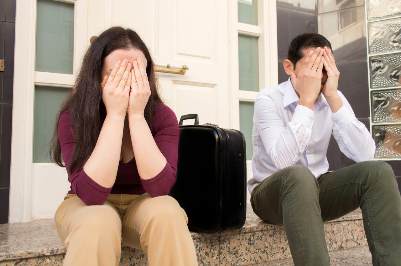 Pareja disgustada sentada en las escaleras con una maleta, enfrentándose a una ejecución hipotecaria. Evitar embargo hipotecario.