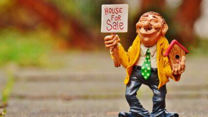 Divertida figura sosteniendo un cartel de "Casa en venta" y una pajarera.